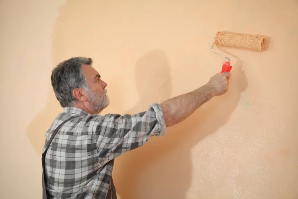 用油漆辊把房子的墙壁涂成橙色的成年工人 — 图库照片