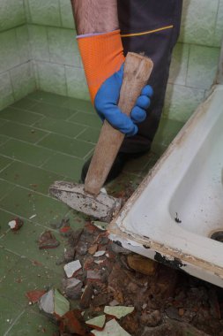 İşçiler yıkılmış bir banyoda eski küveti ve çekiçle döşeyip yıkıyorlar.
