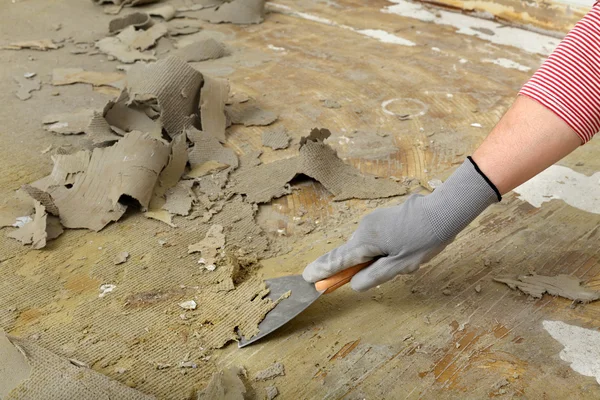 Travailleur utilisant un couteau à mastic pour nettoyer le sol — Photo