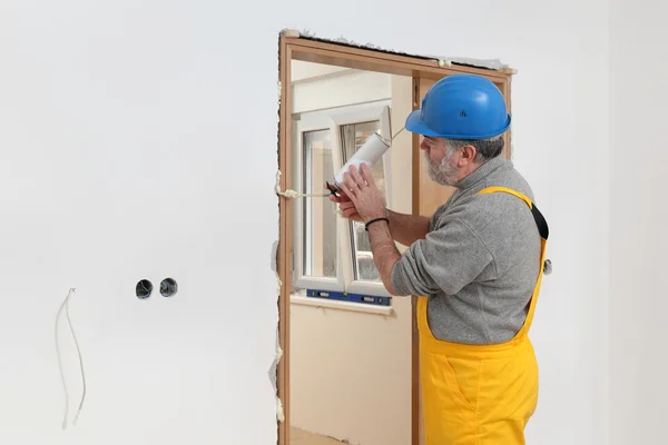 Trabajador instalando puerta de madera, utilizando espuma de poliuretano — Foto de Stock