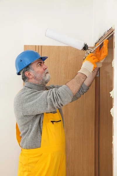 Worker installing wooden door, using polyurethane foam — Stock Photo, Image