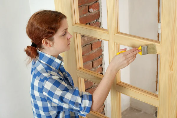 Junge Arbeiterin bemalt neue Holztür — Stockfoto