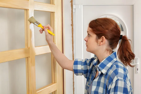 Young girl worker, painting new wooden door — Stock Photo, Image