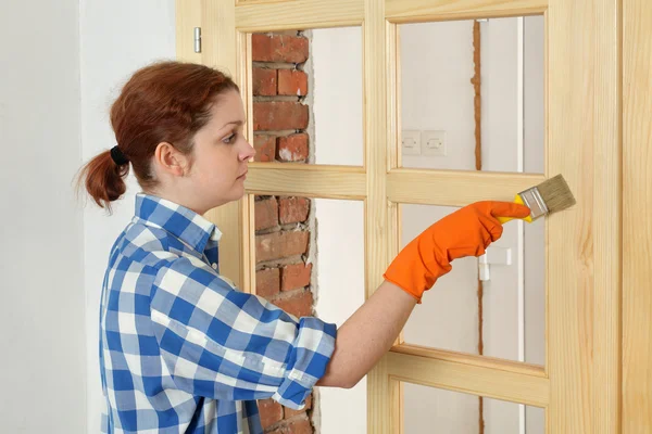 Young girl worker, painting new wooden door — Stock Photo, Image