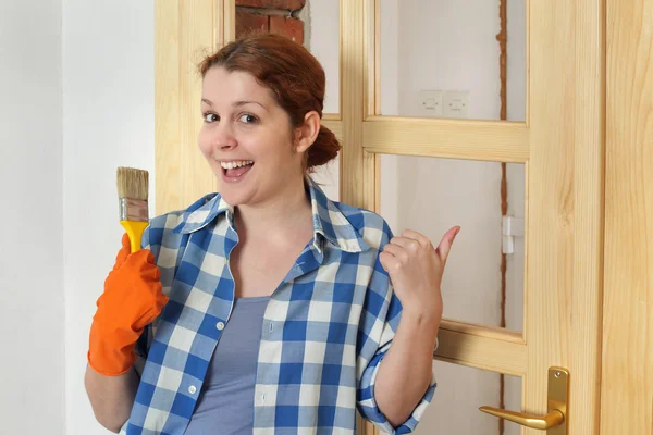 Jonge lachende meisje werknemer, schilderen nieuwe houten deur — Stockfoto