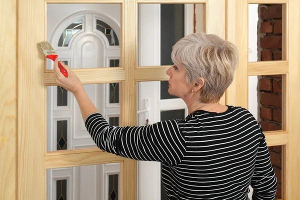 Volwassen vrouwelijke werknemer schilderij houten deur — Stockfoto