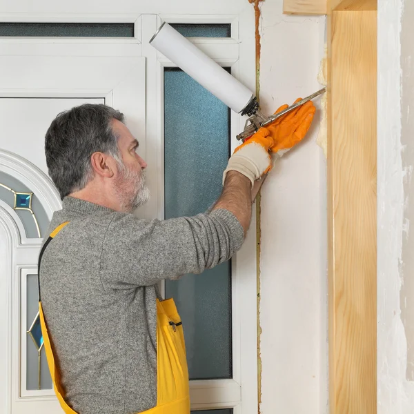 Trabajador instalando puerta de madera, utilizando espuma de poliuretano — Foto de Stock