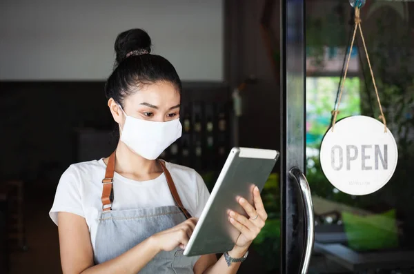Mutlu Taylandlı garson, koruyucu maskeli, elinde tablet, restoranın yeniden açılması, Tayland, Koh Phangan 