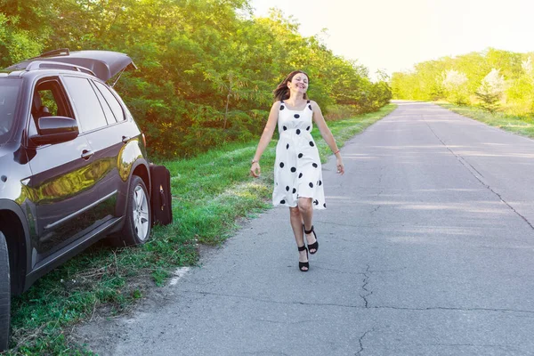 若い女性はロードトリップを楽しんでいます 白いドレスの女の子が笑って車の背景に道路上で踊ります — ストック写真