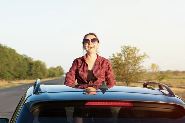 車で旅行 女の子は車のハッチの外を見ている 車の屋根の上に座って人生を楽しむ若い女性は — ストック写真