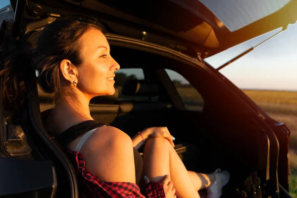 車のトランクに座って道端で夕日を楽しむ幸せな美しい女の子 車の中の若い女性は — ストック写真
