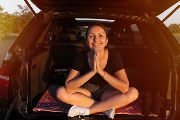 車のトランクに座って道端で夕日を楽しむ幸せな美しい女の子 車の中の若い女性は — ストック写真