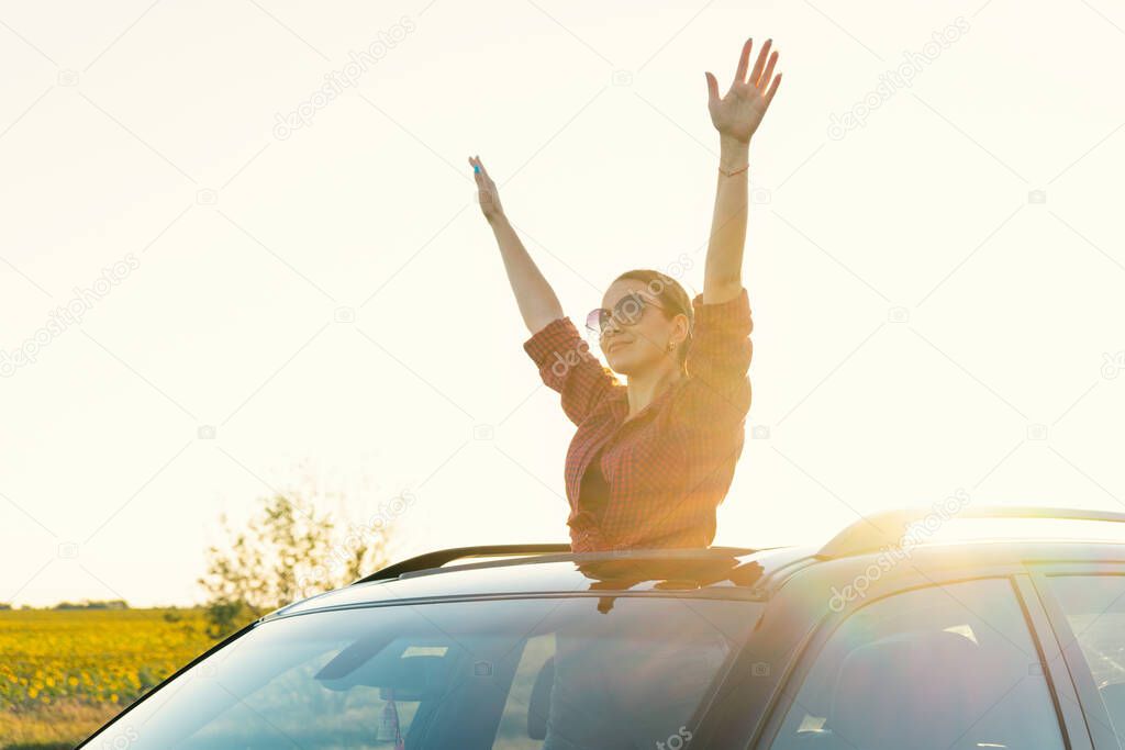 Travelling by car. The girl looks out of the car hatch. young woman sitting on the car roof and enjoying the life