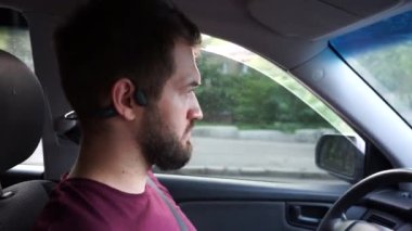 Yakışıklı sakallı genç adam araba kullanıyor ve konuşuyor.