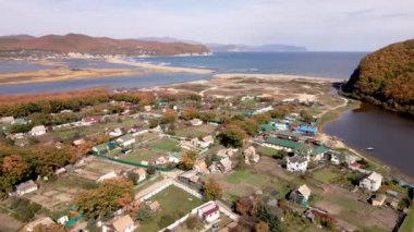 Hava görüntüsü: Kamera Primorsky Bölgesi 'ndeki Smychka deniz köyünün üzerinden uçuyor. Tepelerle çevrili güzel bir göl ve bir Rus köyü.