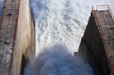 Rusya 'nın Magadan bölgesindeki Kolyma hidroelektrik santrali. Hidroelektrik santralinin barajından sızıntı var. Büyük bir su akıntısı yüksek tepelerin arka planına karşı nehre akar.