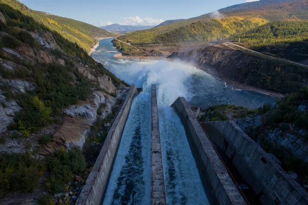 Centrale idroelettrica di Kolyma nella regione di Magadan, Russia. A spirale dalla diga della centrale idroelettrica. Un enorme flusso d'acqua scorre nel fiume sullo sfondo di alte colline — Foto Stock