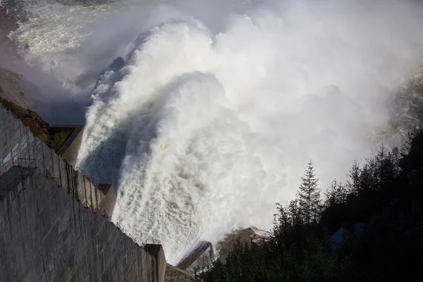 Centrale idroelettrica di Kolyma nella regione di Magadan, Russia. A spirale dalla diga della centrale idroelettrica. Un enorme flusso d'acqua scorre nel fiume sullo sfondo di alte colline — Foto Stock