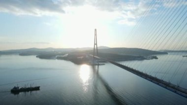 Yukarıdan bak. Bir ticaret gemisi kışın gün batımına karşı Rus köprüsünün altından geçiyor. Rus Köprüsü, Vladivostok 'taki buzlanma ile kapatıldı..