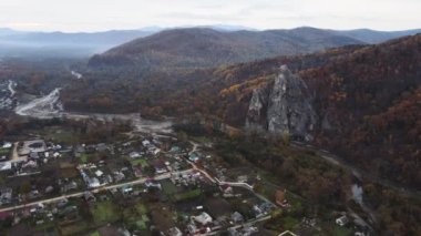 Rus köyünün arka planında yüksek bir resim uçurumu, bir nehir ve bir tepede sonbahar ormanı var. Yukarıdan bak. 4 bin. Primorsky Kray 'deki Kavalerovo köyündeki Dersu Uzala kayası