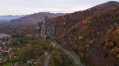 Yüksek bir uçurumun panoramik görüntüsü bir sonbahar ormanının arka planına ve pitoresk bir nehre karşı. Yukarıdan bak. 4 bin. Primorsky bölgesindeki Kavalerovo köyündeki Dersu Uzala kayası..