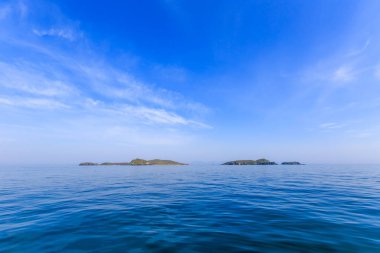 Sakin mavi bir deniz ve mavi gökyüzünün ortasında ıssız yeşil bir ada. Güzel rahatlama arkaplanı