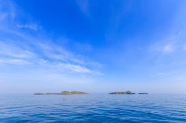 Sakin mavi bir deniz ve mavi gökyüzünün ortasında ıssız yeşil bir ada. Güzel rahatlama arkaplanı