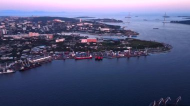 2020 yazı- Vladivostok, Rusya - Top view. Vladivostok 'ta ticari liman. Kamera günbatımında konteynır limanı ve Rus köprüsü manzaralı Golden Horn Körfezi üzerinde uçuyor.
