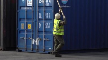 Vladivostok, Rusya - 2020, yaz - Vladivostok ticari deniz limanında çalışıyor. Açık yeşil yelek ve kask giyen bir defin işçisi konteynıra askı takar.