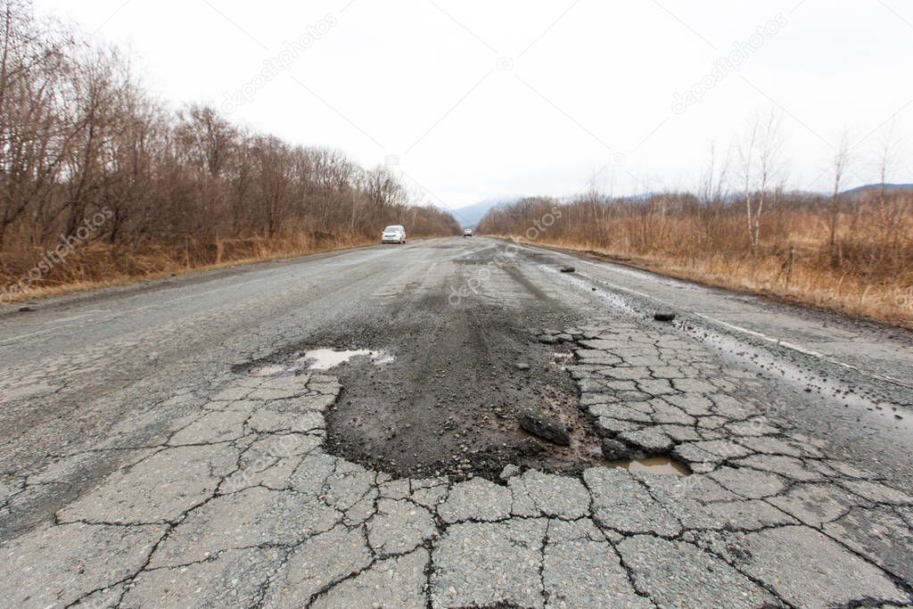 Bad Russian asphalt road. The asphalt road is full of holes and cracks among dried autumn trees