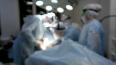 Odaklanamıyorum. COVID-19 koronavirüs salgını sırasında kırmızı bölgede operasyon. Doktorlar ameliyat masasına eğildi ve koruyucu paltolu bir adamı ameliyat ettiler..