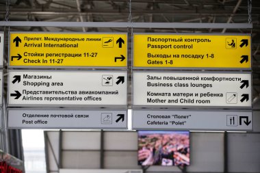 Havaalanındaki sarı bilgi tabelaları yolcu dinlenme yerlerini ve biniş kapılarını gösteriyor. Havaalanı altyapısı