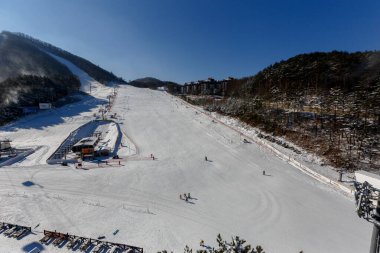Alpencia, Güney Kore, 2016 - 2018 Kış Olimpiyatları için Olimpiyat Köyü. Turistler kayak ve snowboard yapıyor kayak pistinin güzel, karlı yamacında.