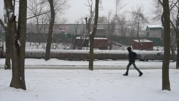 ウラジオストク プリモルスキー地方 2021年 スローモーション 雪の中を通りすがりの車を背に若者が歩道を歩いている — ストック動画