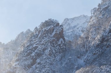 Mavi gökyüzüne karşı resimli kar kaplı kayalar. Erişilemez dağlar şiddetli bir kar fırtınası sırasında karla kaplıdır. Kaya tırmanışı