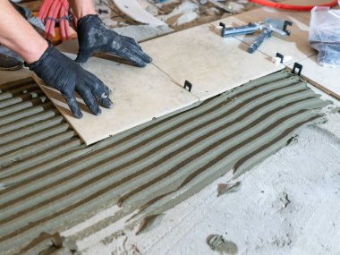 Seramik fayansları döşeyen usta işçiler yeni apartmanın inşaat alanında döşeme yapıyor.