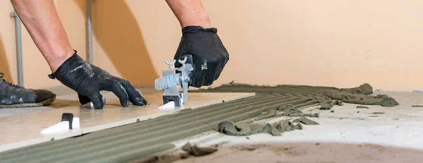 Los trabajadores están utilizando abrazaderas de plástico y cuñas para nivelar la baldosa de cerámica en el suelo. Sistema de nivelación de azulejos. Banner. Imagen de archivo