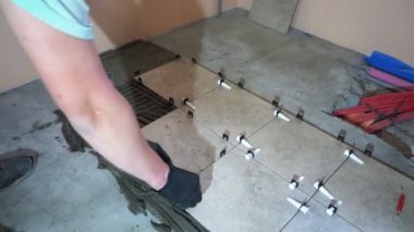 Bir işçi seramik fayansı takoz ve klipslerle düzleştiriyor. Döşeme seviyelendirme sistemi