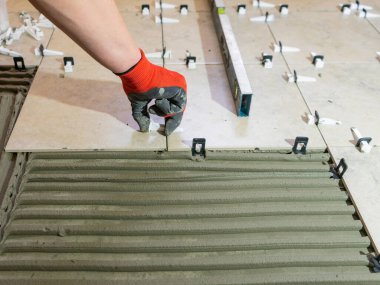 İşçilerin elleri seramik fayanslarla ve tiler için aletlerle. Döşeme döşemesi. Seramik fayans zemin yapıştırıcı, havan topu, seviye.