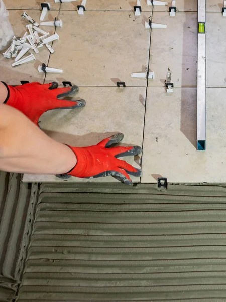 Workers hands with ceramic tiles and tools for tiler. Floor tiles installation. Ceramic tile floor adhesive, mortar, level. — Stock Photo, Image