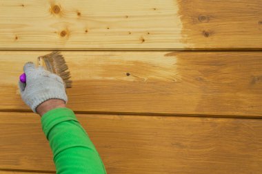 Eldiven giymiş bir işçi eli, ahşap bir ev boyuyor. Ahşap bir evi koruyucu bir bileşikle kaplamak..