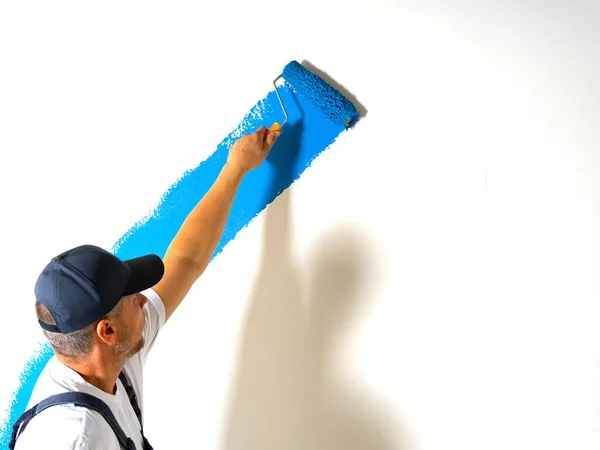 Erkek Ressam Mavi Renkli Silindirli Beyaz Bir Duvar Boyuyor — Stok fotoğraf