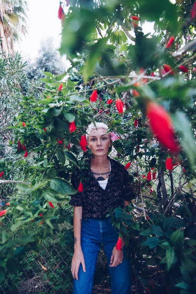 สาวผมบลอนด ในสวนใกล นไม ดอกไม แดง — ภาพถ่ายสต็อก