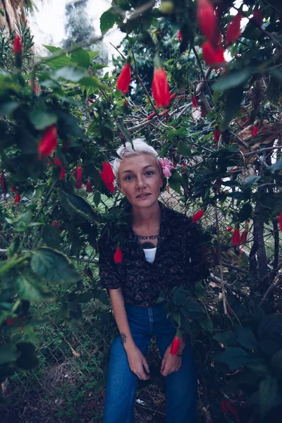 สาวผมบลอนด ในสวนใกล นไม ดอกไม แดง — ภาพถ่ายสต็อก