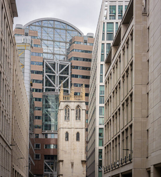 Old church tower amidst new modern ofice buildings in the city of London, UK