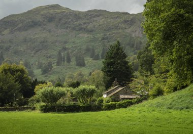 Arka planda bir dağ olan Cumbria, İngiltere 'deki Cumbria Gölü' ndeki taştan kulübe manzarası.