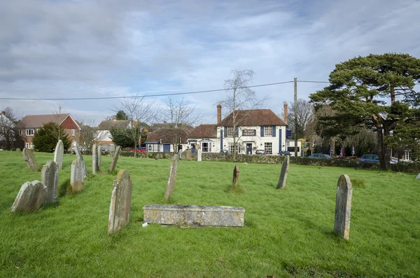 Gravstenar på en kyrkogård med byn puben i bakgrunden — Stockfoto