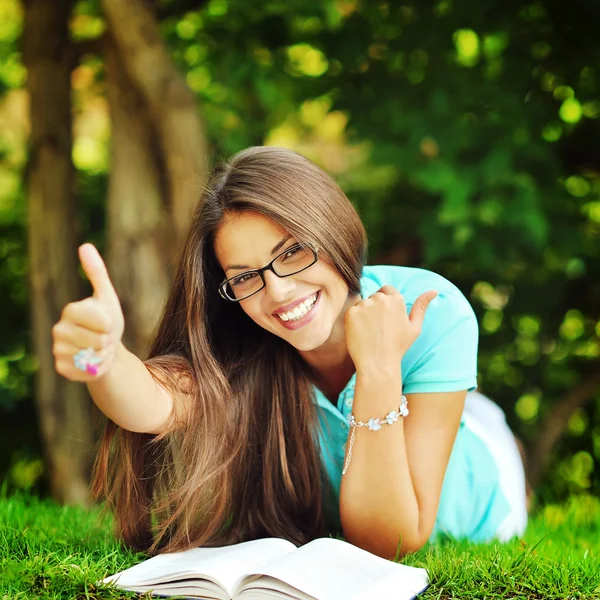 Happy smiling girl in glasses lying in the park near a book and Stock Image