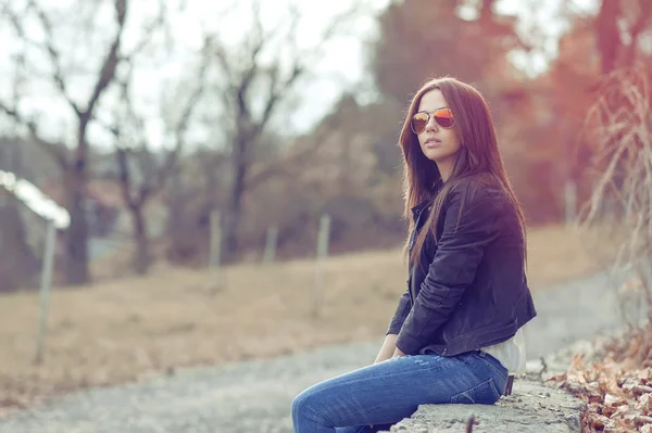 Jonge sexy brunette vrouw in jeans, jas en zonnebril poseren — Stockfoto