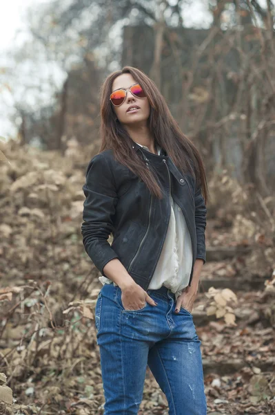 Mulher morena sexy nova em jeans, jaqueta e óculos de sol posando — Fotografia de Stock